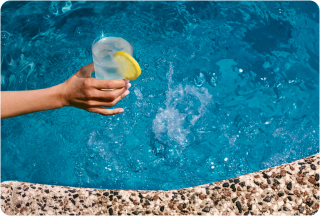 Person holding a drink by the pool